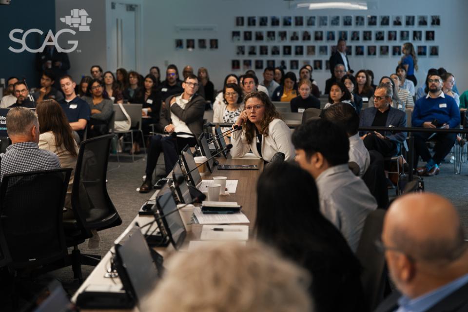 Meeting with diverse people seated at tables, discussing attentively in a brightly lit room.