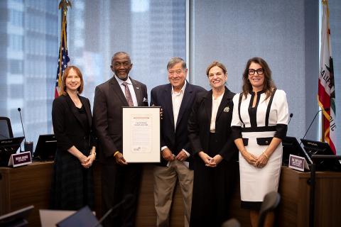 Group of five people smiling, one holding a framed certificate in a conference room.